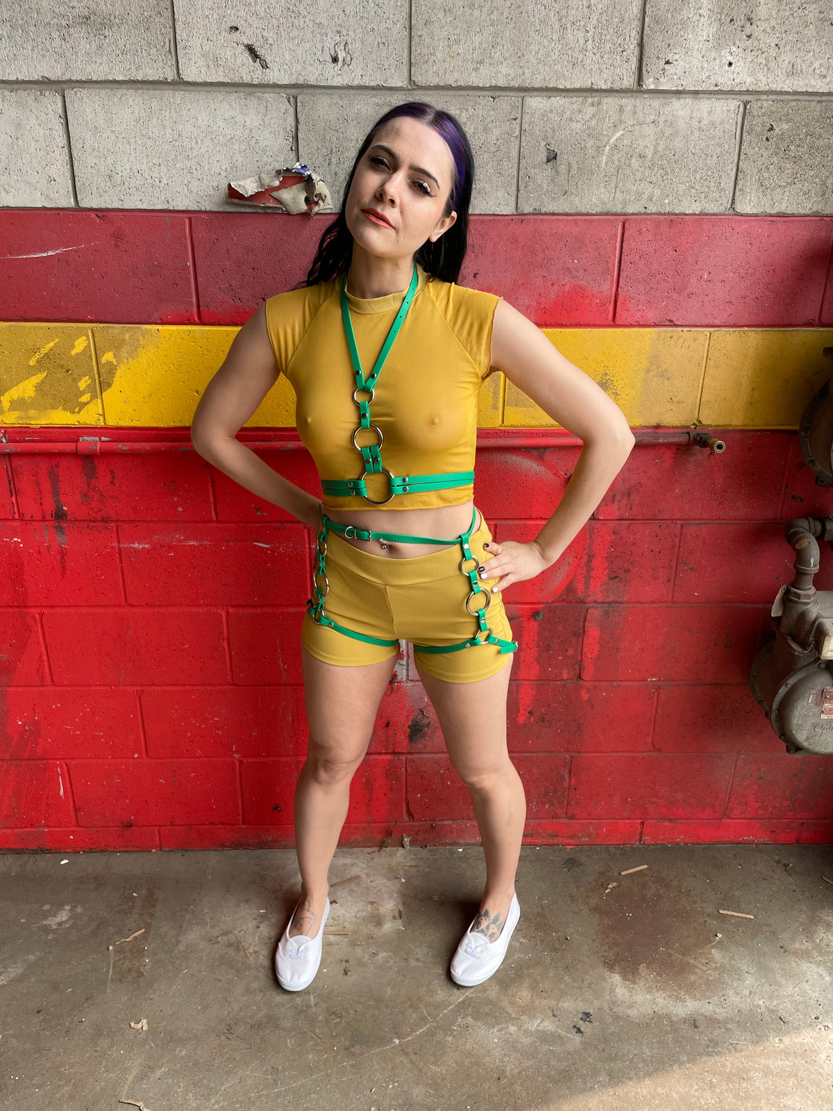 Woman wearing a green thigh harness set over a yellow top and shorts.