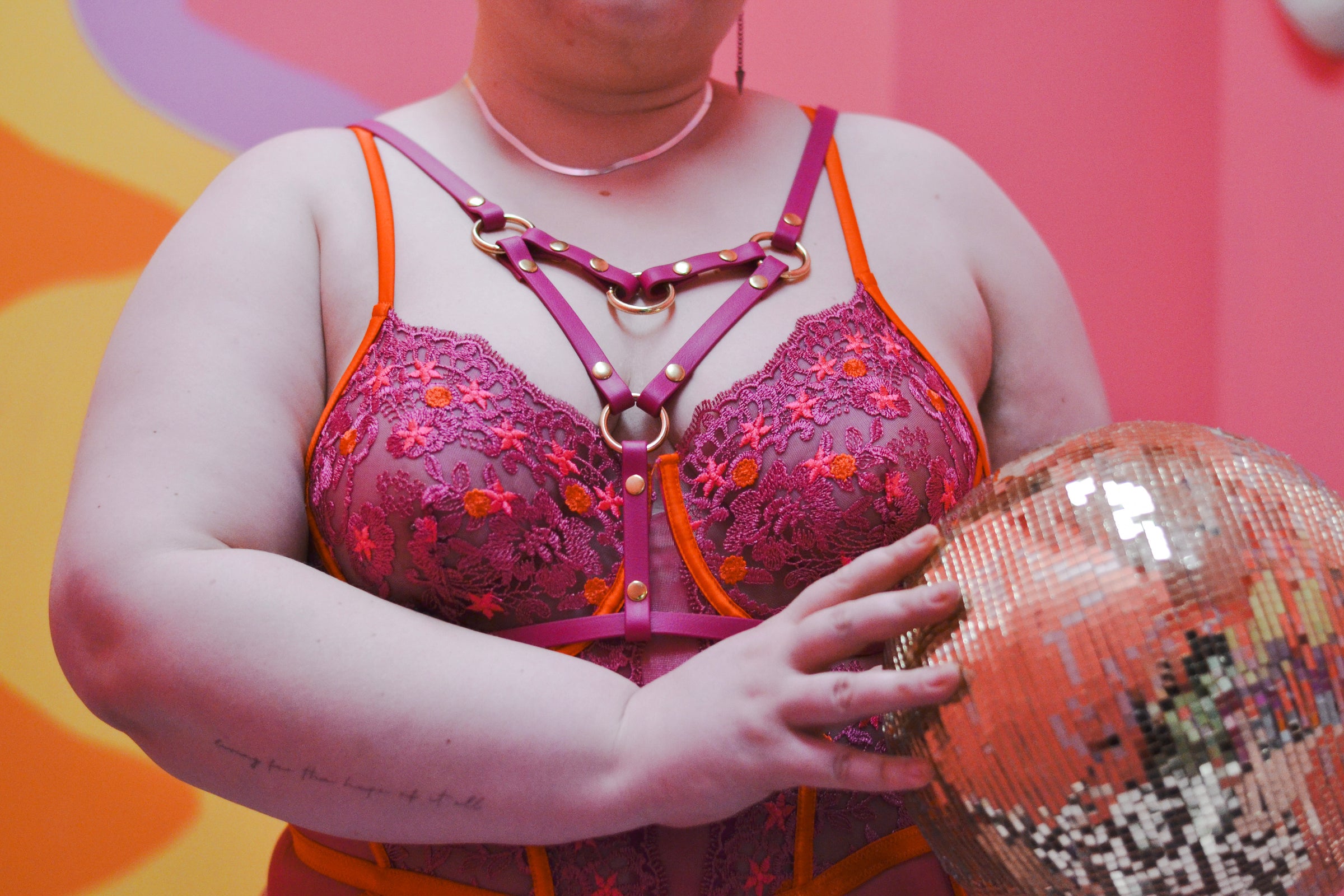 Closeup shot of person holding a disco ball and wearing the magenta angle grinder harness over their pink bodysuit.