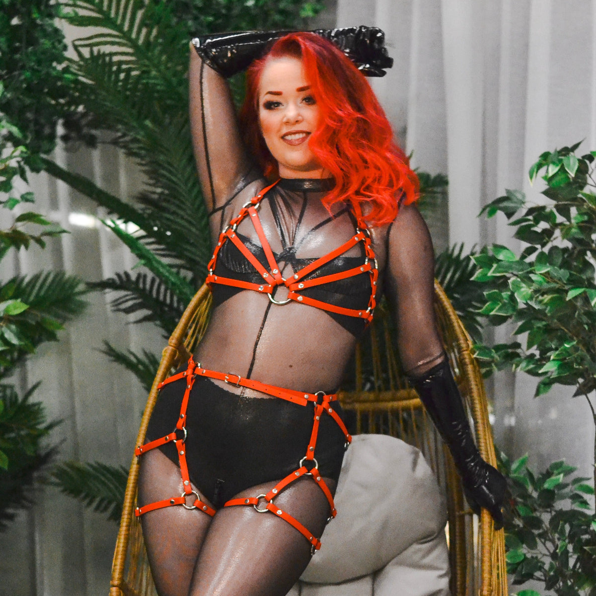 Woman with red hair wearing a black catsuit and a red thigh harness over it.