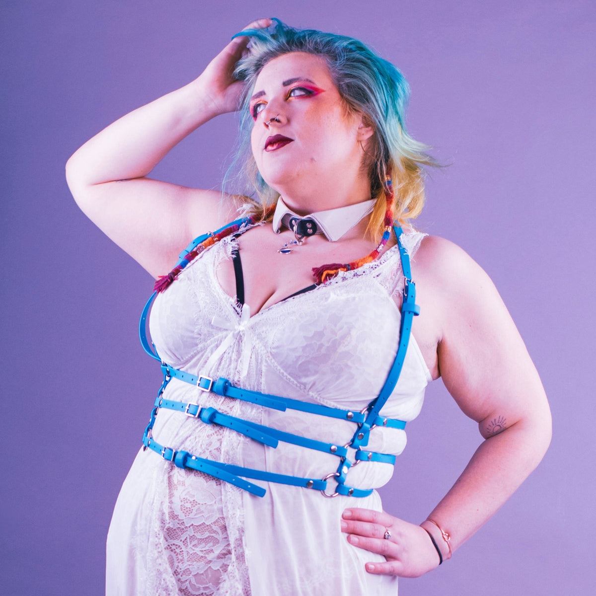 Woman wearing white lingerie with a turquoise body harness over it.