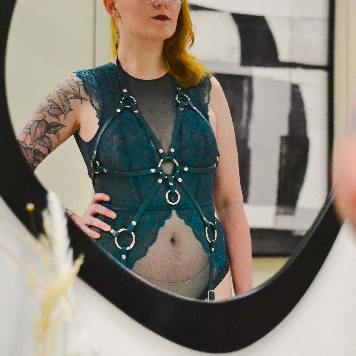 Reflection of a person in green lace with a green full body harness over the lingerie.