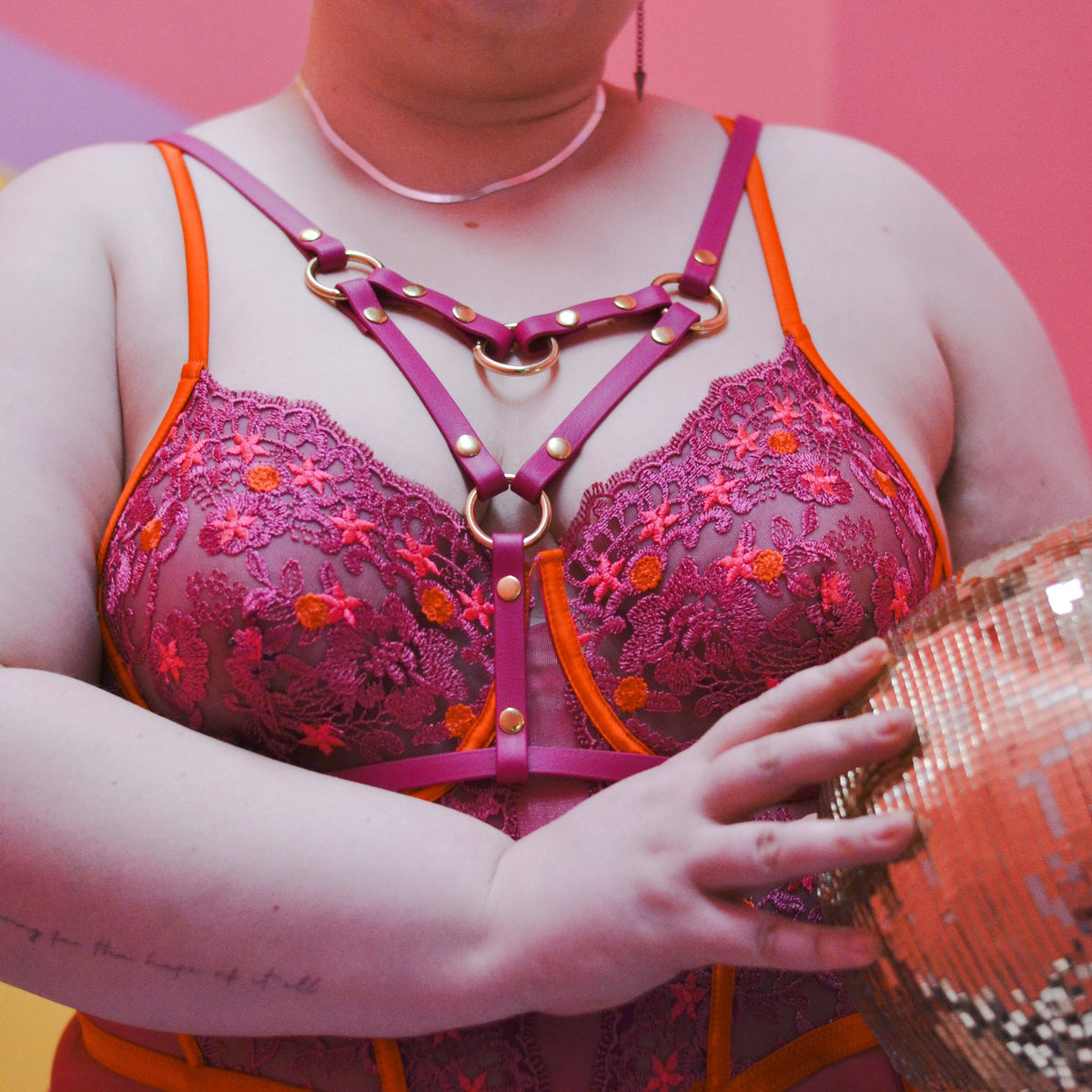 Image of a woman cropped at the neck wearing a lace body suit with a magenta angle grinder harness.