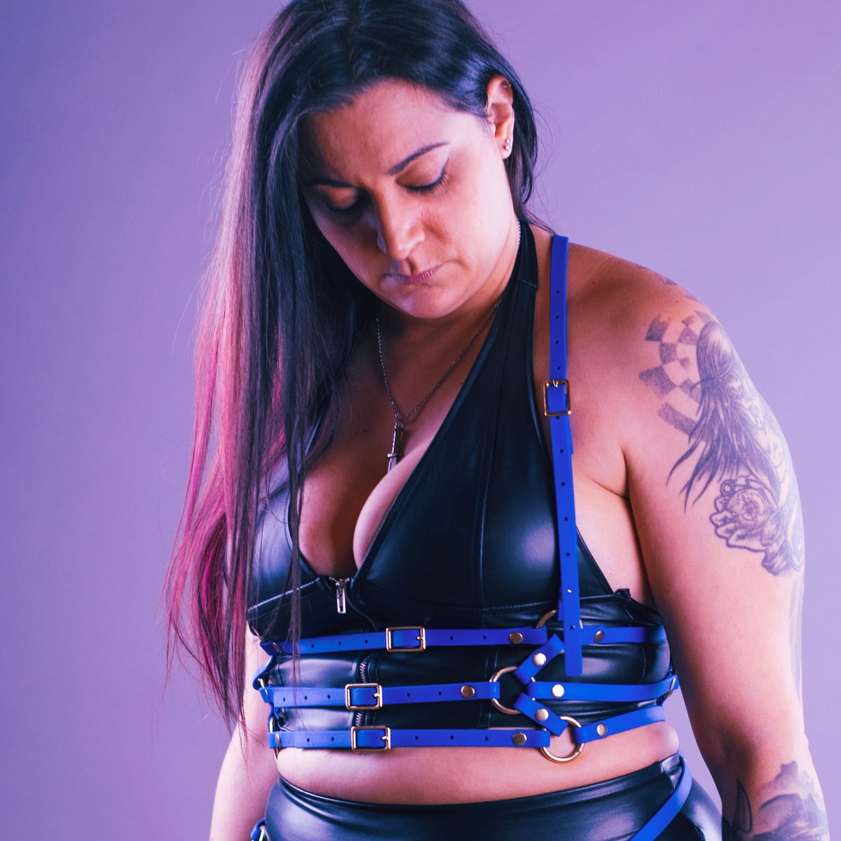 Woman wearing an electric blue waist harness over her black leather look top.