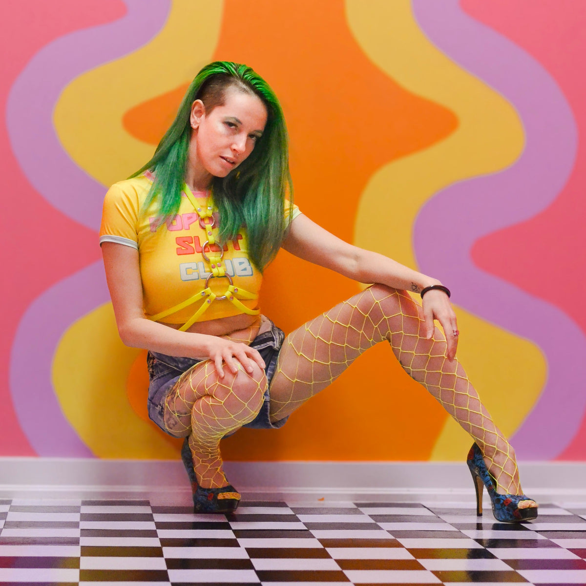 Woman crouching wearing a neon yellow waist harness over her colourful outfit.