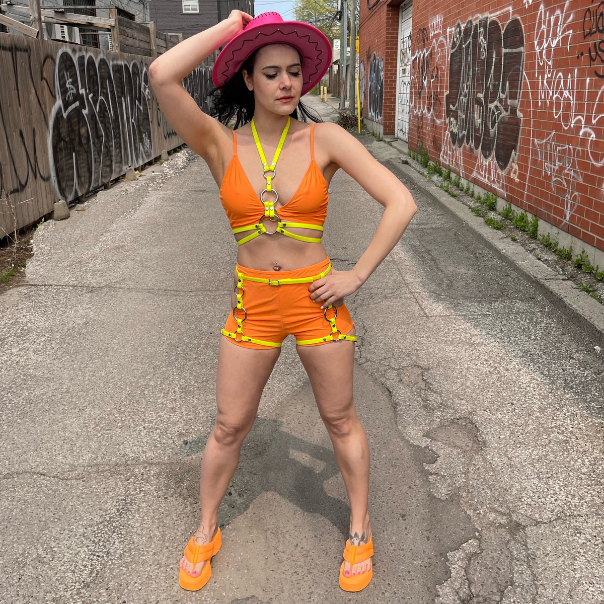 Neon yellow leg harness outfit  on a woman wearing an orange top and shorts set and a pink hat.