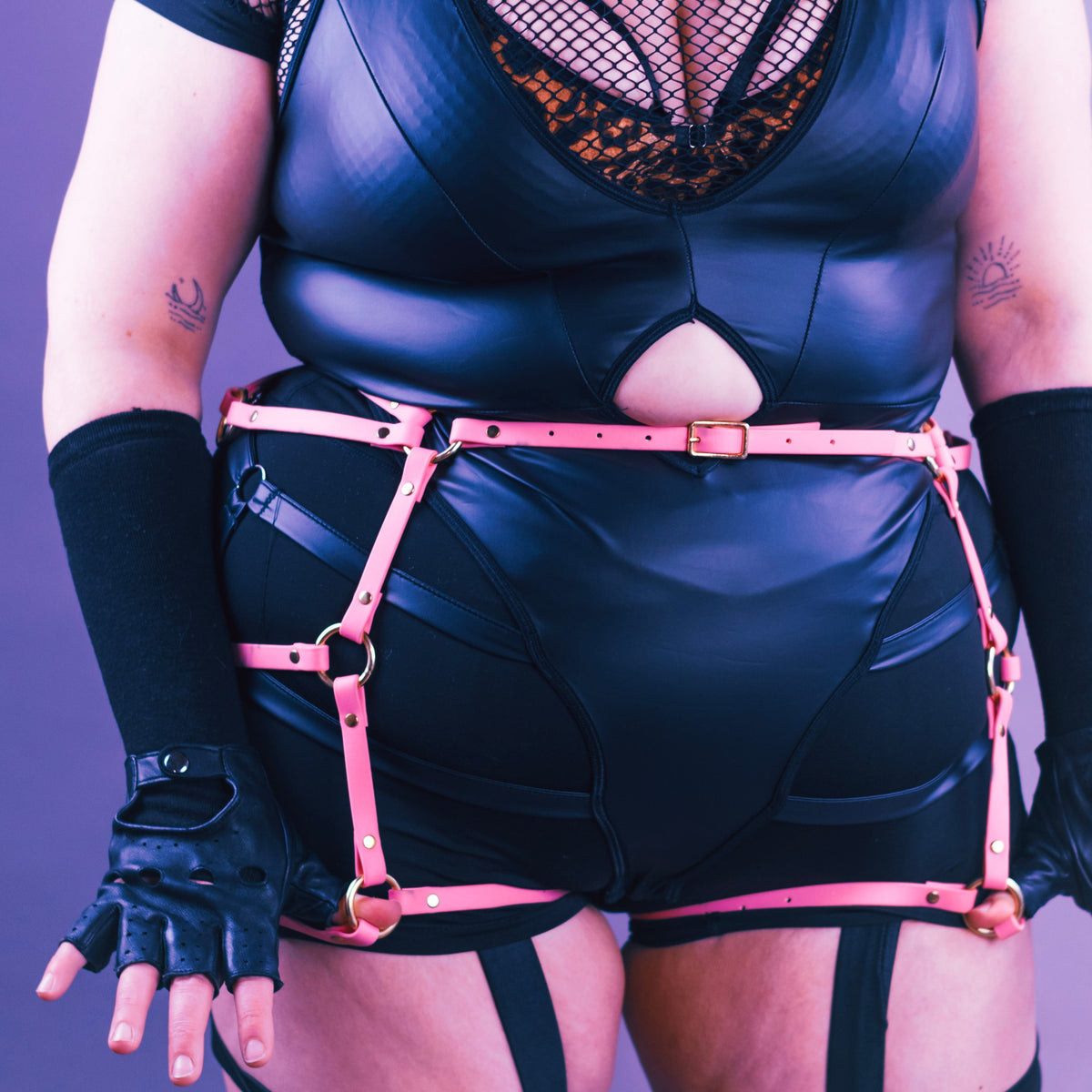Closeup shot of woman wearing black with a pastel pink thigh harness over her bottom.