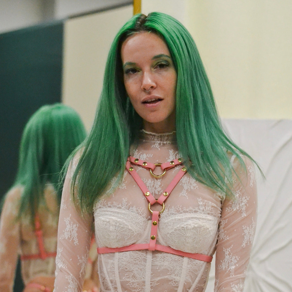 Person wearing ivory lingerie and a pastel pink chest harness with brass hardware. 