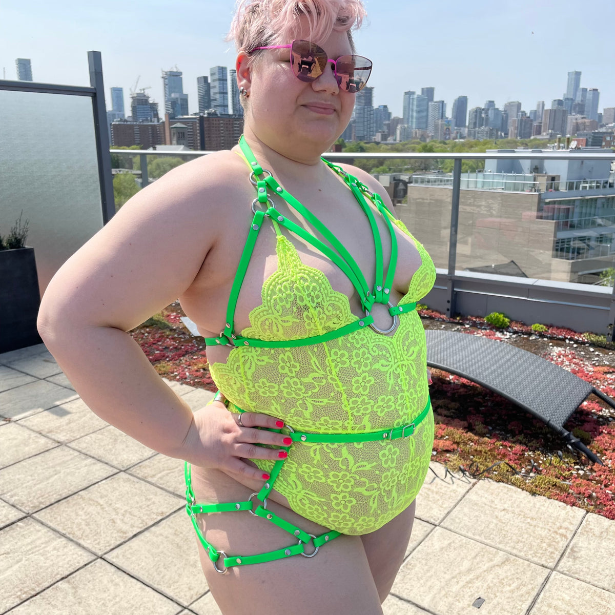 Woman outside with short hair wearing a neon body suit with a lime green sexy butt harness and a plus size bondage bra
