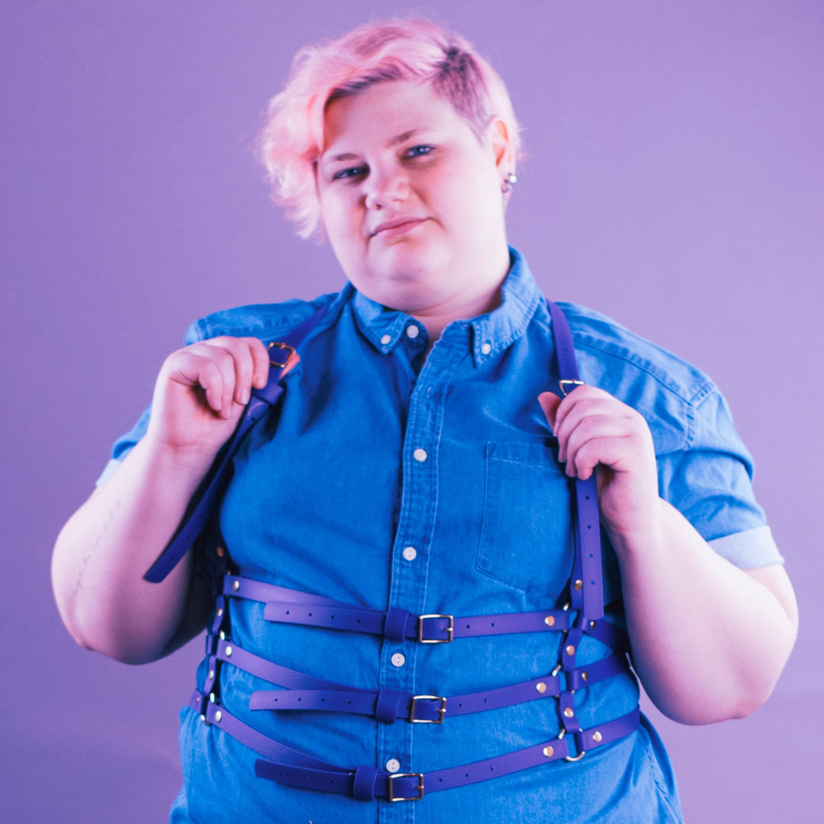 Woman wearing a purple suspender style harness over a denim shirt.
