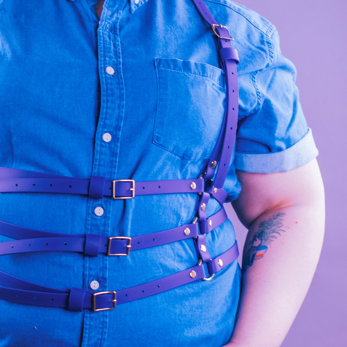 Person wearing a purple vegan harness over a chambray shirt.