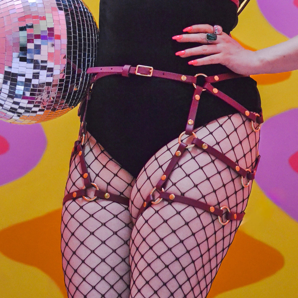 Closeup shot of a woman in black fishnet stockings wearing a burgundy red thigh harness over her outfit.